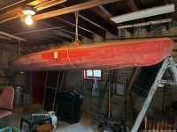 Side view of red wooden boat hull suspended in garage