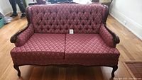 Front view of Victorian antique settee showing tufted backrest and patterned red upholstery with carved wooden arms and legs