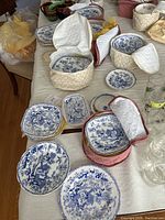 Overview of 2 quilted fabric carriers holding stacked blue Mikado pattern bowls, plus loose plates and dishes laid out on table