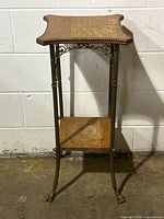 Front angle view of the antique solid oak plant stand table showing the top and lower shelf with brass claw feet and decorative metalwork.