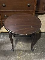 Round mahogany coffee or end table showing top surface and legs with wear spots and scratches.