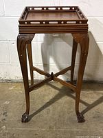Full front view of the antique walnut pedestal table showing raised gallery top, Queen Anne legs, and ball and claw feet with cross stretcher support.