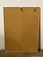 Front view of the rectangular cork board with oak frame leaning against a white wall, showing surface and frame details.