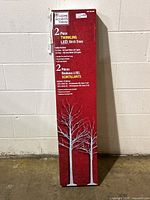 Box front showing 2-piece set of twinkling LED birch trees with dimensions and branding.