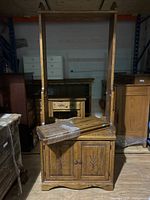 Front view of antique style oak bookshelf by House of Brogham showing frame, lower cabinet with carved doors, and 3 wrapped adjustable shelves leaning against it.
