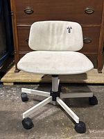 Front view of white fabric rolling office chair with metal base and caster wheels, showing wear and stains on upholstery