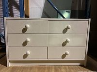 Small off white chest of drawers with 6 drawers, photographed frontally showing the drawer layout and condition.