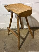 Front angled view of vintage handmade wood stool showing natural edge carved log seat and three splayed legs with stretcher.