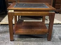 Wood coffee table with beveled glass top and brass tone corners, shows some surface wear and scratches. Lower wood shelf is visible.