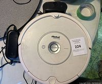 Top view of the iRobot Roomba robotic vacuum cleaner showing the CLEAN button and surrounding controls with charger and power cable beside it.