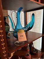 Photo of blue glass abstract sculpture with multiple curved arms and hollow body on shelf