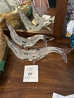 Side view of two clear and black Murano glass seal figurines placed on wooden surface with mirror reflection.