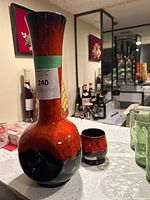 Tall ceramic MCM style vase with red and black glaze and small matching glass, displayed on a kitchen counter.