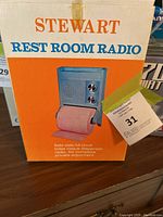 Photo of the original packaging box for Stewart Rest Room Radio featuring the image of the radio mounted above the toilet paper holder.