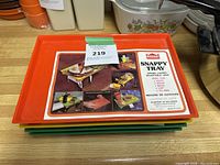 Photo showing stacked orange, yellow, and green Blesscraft Snappy Trays with product leaflet on top providing product info and uses.
