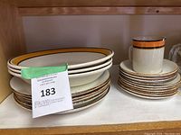 Side view of stacked dinner plates and smaller plates with a stoneware mug stacked on smaller plates. Labels with lot numbers are visible.