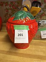 Front view of the strawberry shaped sugar/cookie jar with lid, showing the detailed texture and bright red color.