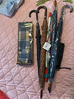 Photo showing six umbrellas in varying styles alongside a gift box containing a checkered scarf