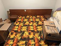 Full front view of assembled bed frame with headboard, nightstands, patterned mattress, cardboard boxes around