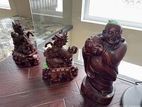 Photo showing all three figures: two dragons and one laughing Buddha, set on wooden surface near window.