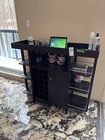 Front view of black wooden bar cart showing bottle storage grid and cabinet with side shelves and top tray.
