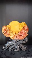 Front view of round yellow-orange stone carving with detailed flowers on a decorative wooden stand.