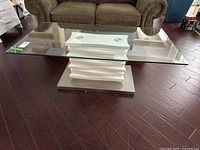 Overall view of rectangular glass coffee table in front of brown upholstered armchair, showing glass top and base structure