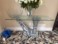 Front angled view showing clear glass rectangular top resting on silver sculpted composite base with abstract design.