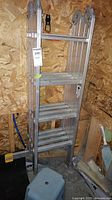 Full view of folded aluminum extension ladder with multiple sections and rectangular steps, displayed in a garage.