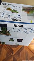 Box of Fluval Edge aquarium showing brand, series and capacity indications (23L/46L) alongside images of planted aquascapes