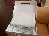 View of white plastic Apple MacBook laptop in its original boxed packaging with charger cable wrapped and placed inside.