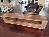 Front view of long wood-finish media cabinet showing three central drawers and open shelf spaces on both sides.