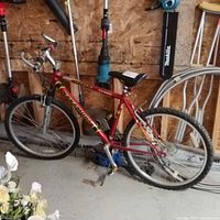 Side view of the red Nakamura 7005 S mountain bike leaning against a wall with various tools and items in the background.