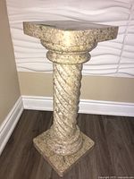 Full front view of beige stone pedestal against wall