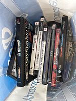 View of multiple PlayStation and PlayStation 2 game cases inside a bag showing spines and partial covers revealing titles like Gran Turismo 4, Dance Factory, Tekken 5, Bases Loaded, Joker 2, and a Japanese title.