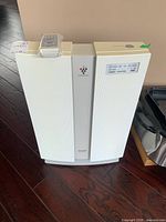 Front view of Sharp PlasmaCluster air purifier with remote control on top wrapped in plastic