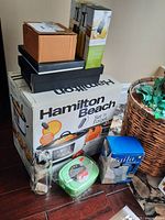 Photo showing Hamilton Beach slow cooker box, Laila moka espresso maker box, green lunch container sealed in plastic, and glass oil and vinegar set.