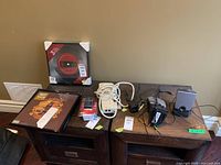 Wide shot showing three LP album frames (two stacked and one upright) and collection of electronics including converter, extension cord, and two small speakers on a wooden surface.