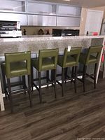 Front view of four bar stools aligned at kitchen counter, showing upholstery color, backrests, and frames