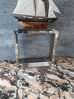 Front view of mirrored stainless steel frame console table with glass top and model ship on top.