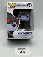 Front view of boxed Funko Pop! Overwatch Widowmaker #94 figure showing character in packaging with branding and figure visible.