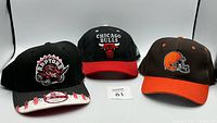 All three baseball caps displayed side by side: Chicago Bulls, Toronto Raptors, Cleveland Browns