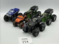 Five assorted monster trucks arranged together showing various colors and designs, including Batman-themed and flame decals.
