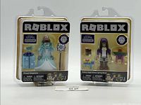 Two Roblox collectible figures in blister packs, Frost Empress and Spring Break figure, showcasing front packaging and exclusive virtual item indication.