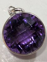 Close-up front view of round purple amethyst pendant set in 10K gold bezel with bail showing.
