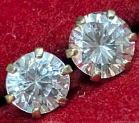 Close-up front view of a pair of round cubic zirconia stud earrings in gold prong settings on red background.
