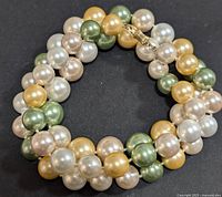 Full view of the coiled pearl necklace showing the alternating patterns of white, green, and golden pearls.