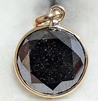Front view of round black diamond bezel-set in 10K yellow gold pendant