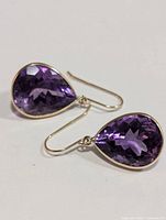 Pair of pear-shaped faceted purple amethyst drop earrings set in yellow gold bezels with hook-style ear wires.