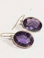 Pair of certified 10K yellow gold earrings each with large oval faceted amethyst stones, deep purple in color, set in bezel mount and hanging from simple gold hooks.